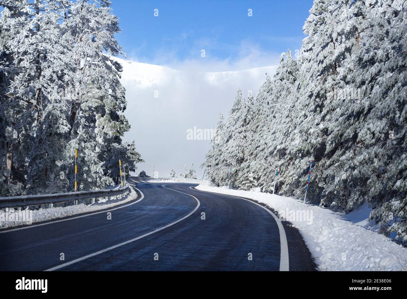 Lonely winding road in a snowy mountain landscape on a sunny winter day. Getaway by car concept. Road trip. Stock Photo