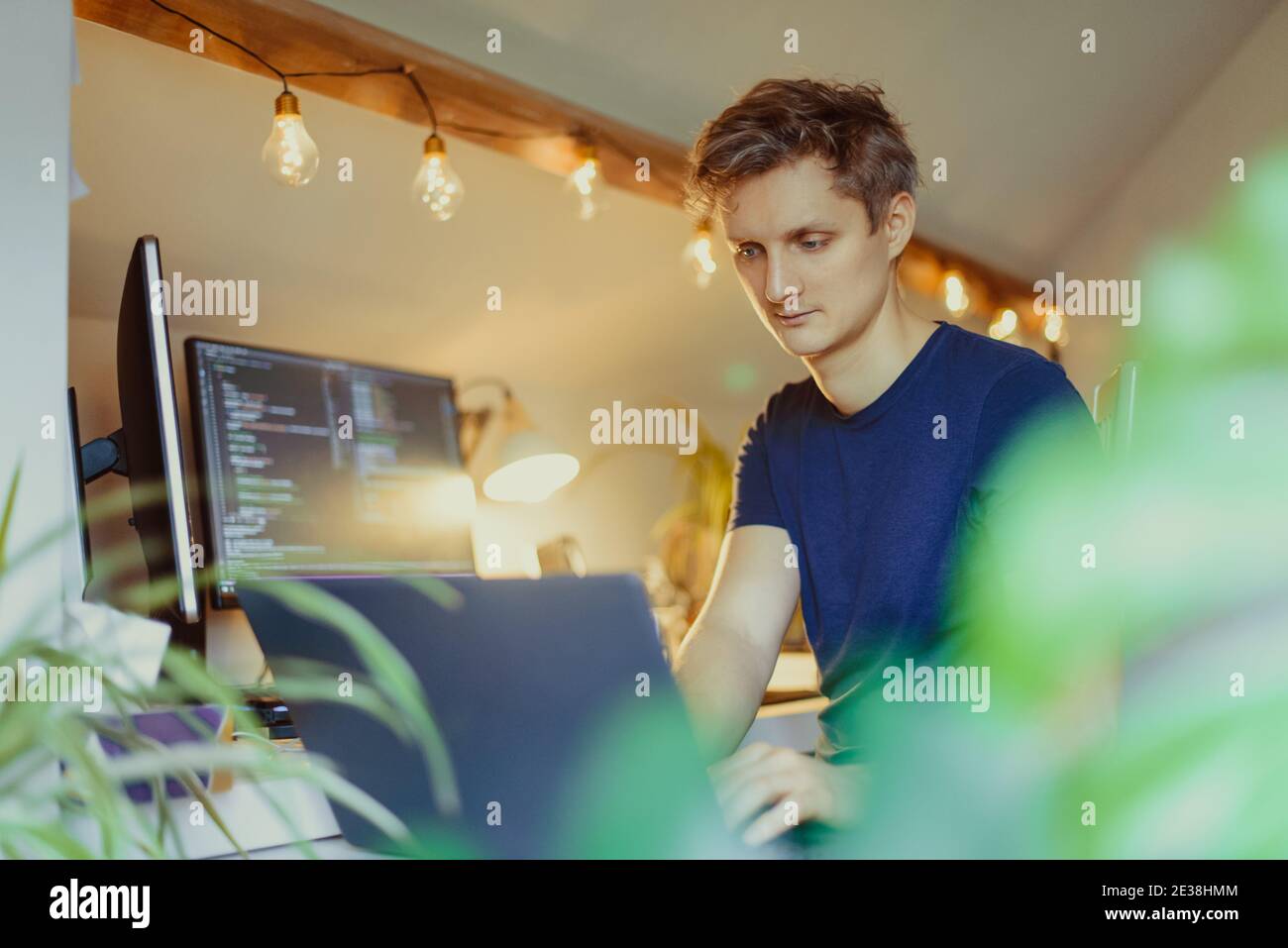 A man sitting at a desk working from home on his computer. IT specialist programmer writing code on his pc and laptop. Developer remote home office Stock Photo