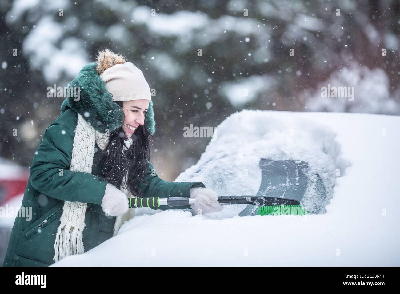Woman struggles to scrape ice and snow off the snowed-in car on a parking lot. Stock Photo