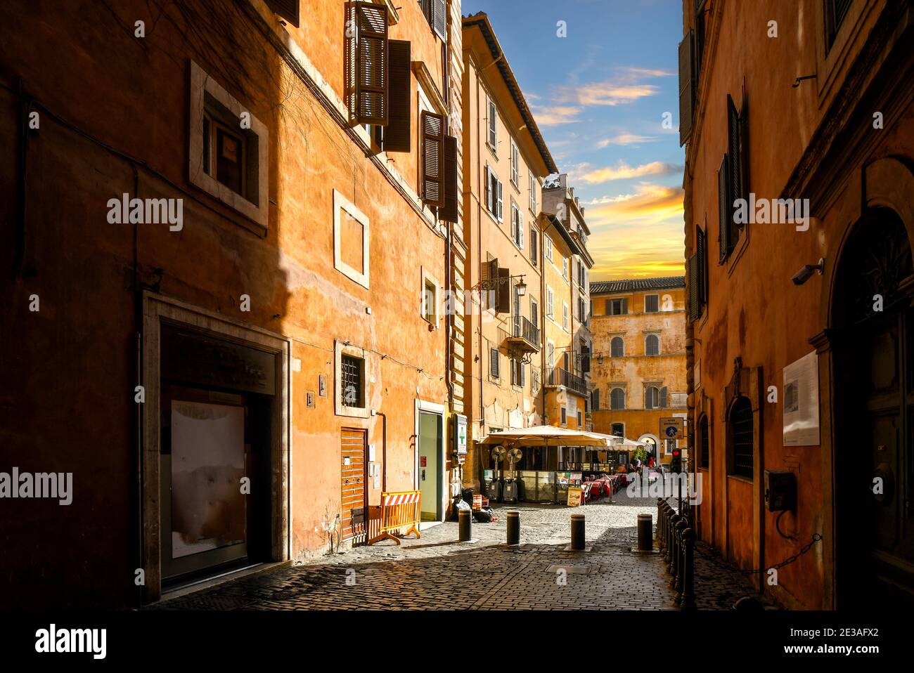 A narrow back alley in the historic center of Rome, Italy, leads to a small sidewalk cafe at sunset. Stock Photo