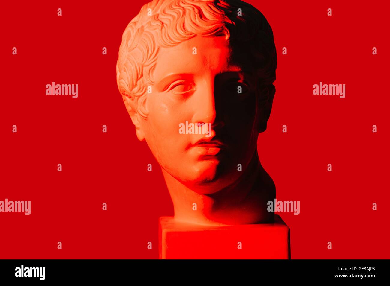 Red-lit half-shaded marble head of young man over red background. Stock Photo