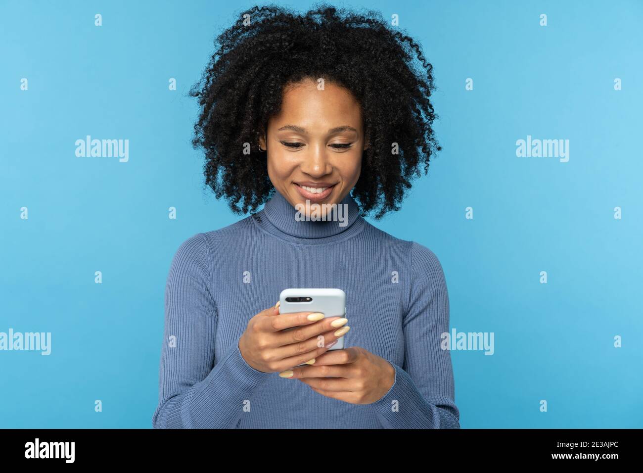 Happy African millennial woman with curly hair chatting in social media, using mobile phone isolated Stock Photo