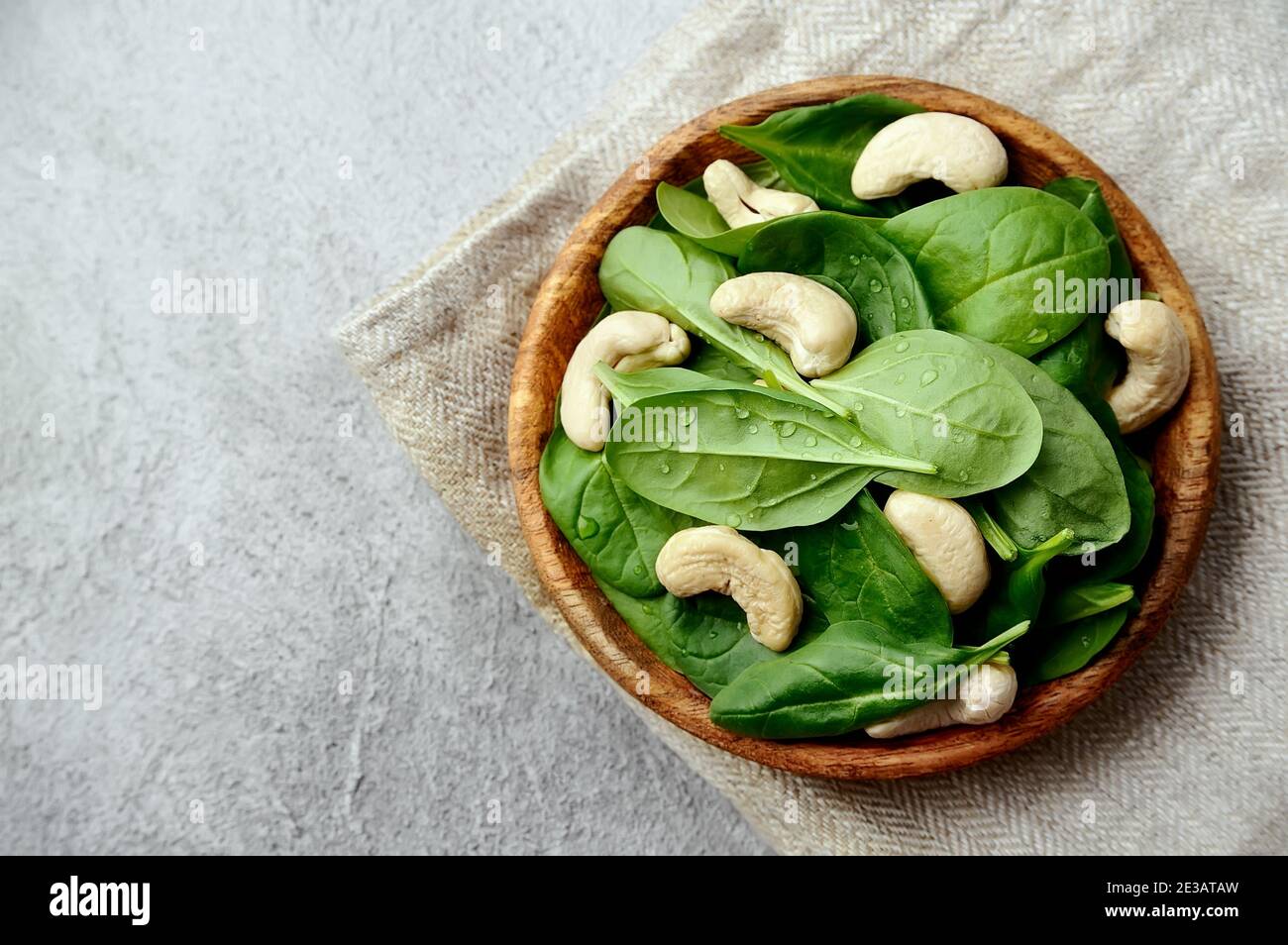 Fresh spinach sald with cashew nuts in wooden plate on concrete tables. Stock Photo