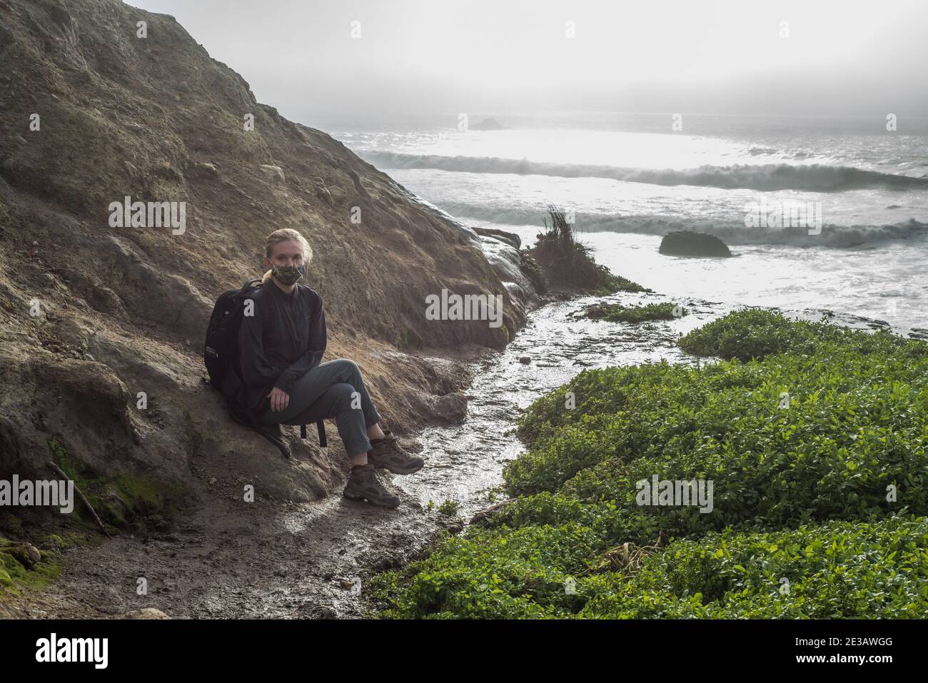 A female hiker sitting on the California coast right above Alamere falls where it tumbles in the Pacific ocean. Stock Photo