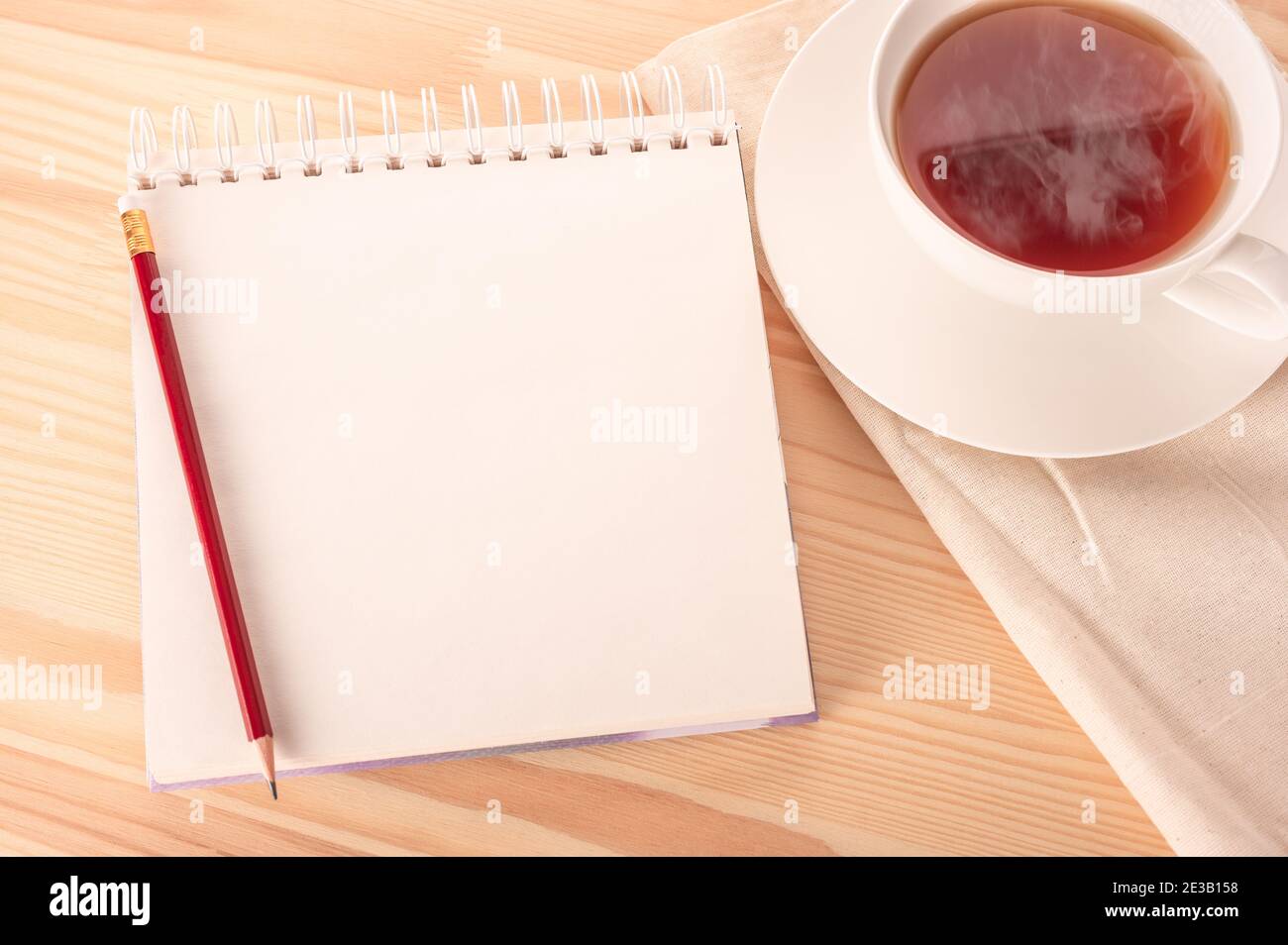 mock up image notebook with blank white page with red pen on wooden table and hot cup of tea. Notepad on a wooden table. copy space. Stock Photo