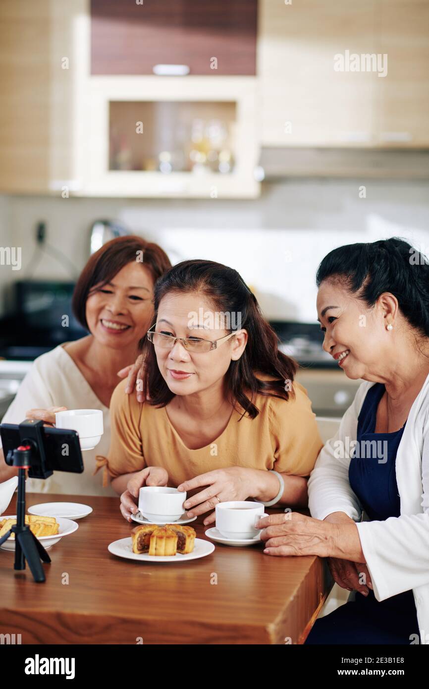 Smiling elderly Asian women drinking tea with pastries and recording video  for their channel Stock Photo - Alamy