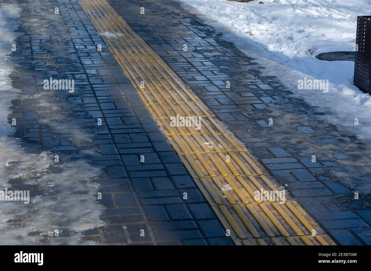 An empty winter sidewalk with a yellow band of tactile tiles. Special tiles that indicate the direction of movement for people with visual problems. B Stock Photo