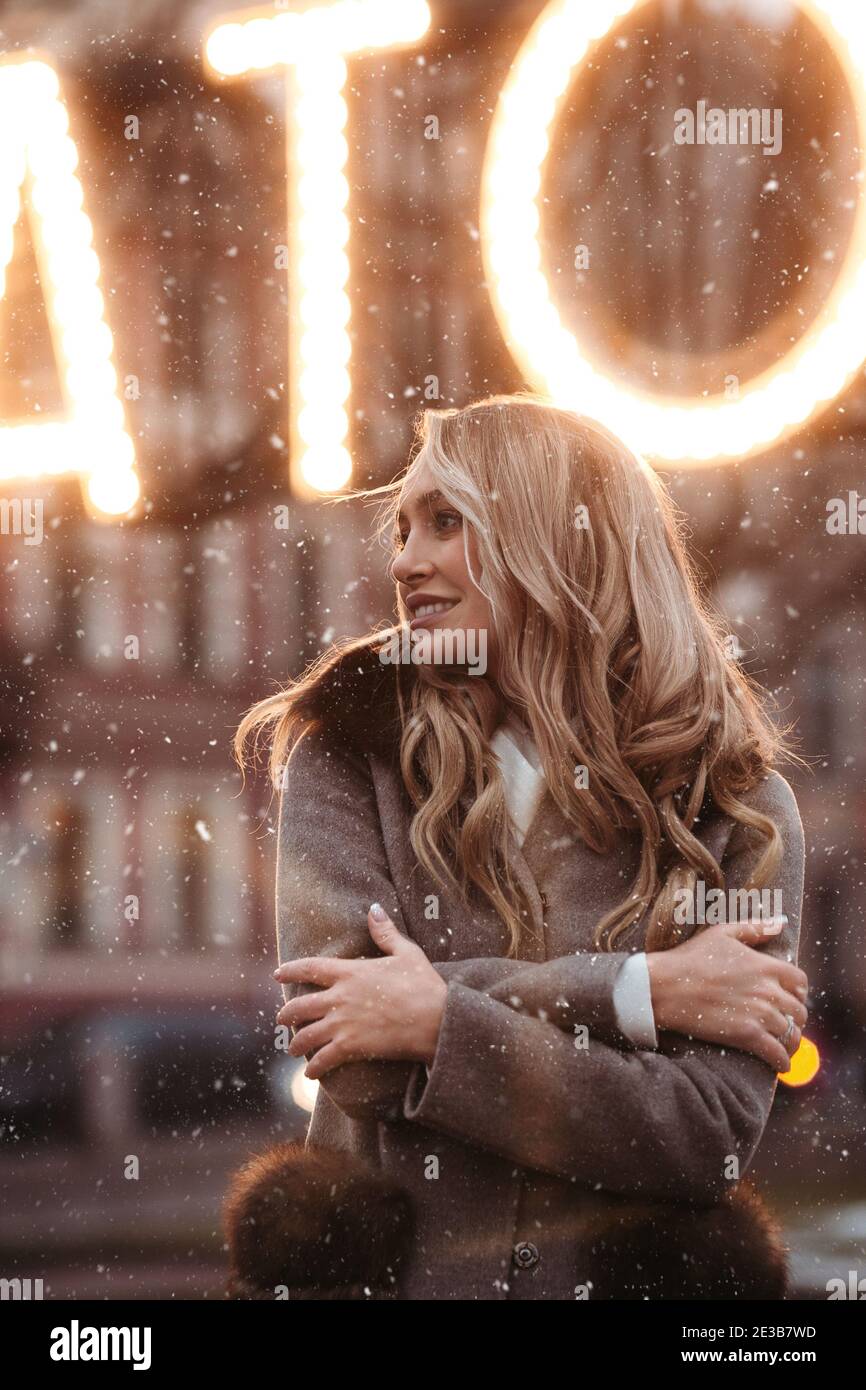 Fashionable happy caucasian woman with blonde wavy hair wear warm coat standing in snowy weather Stock Photo
