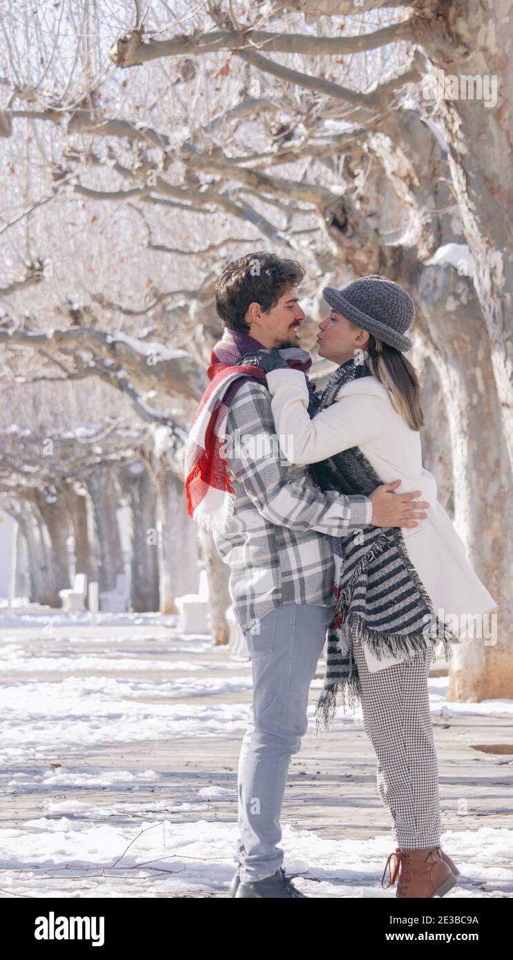 Young couple hugging and kissing on a snowy winter park near of a many big trees full of snow. Concept of joint rest. Winter Photography 2021. Stock Photo