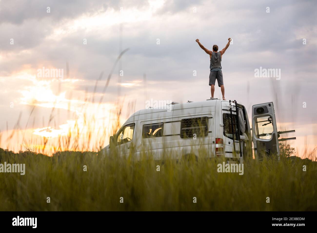 Man with raised arms on top of his camper van Stock Photo