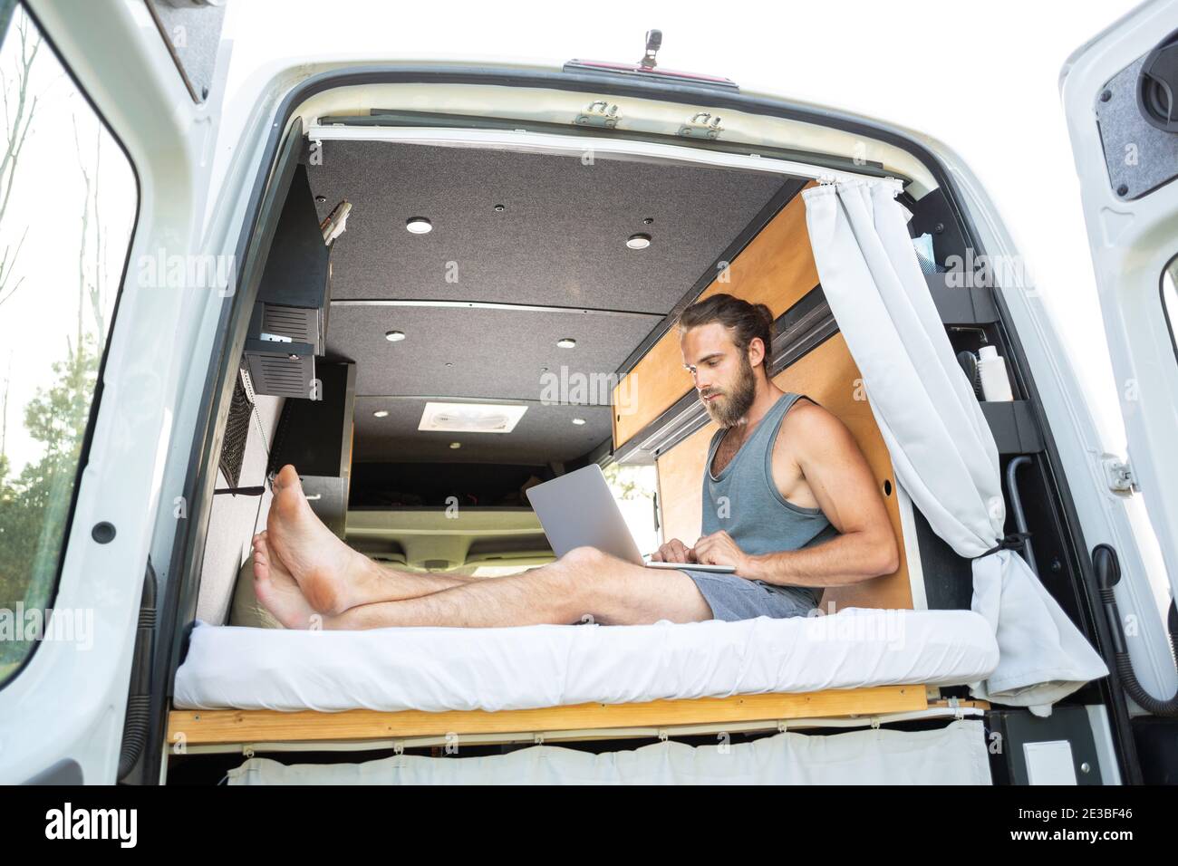 Man relaxing inside his camper van uses a laptop computer Stock Photo