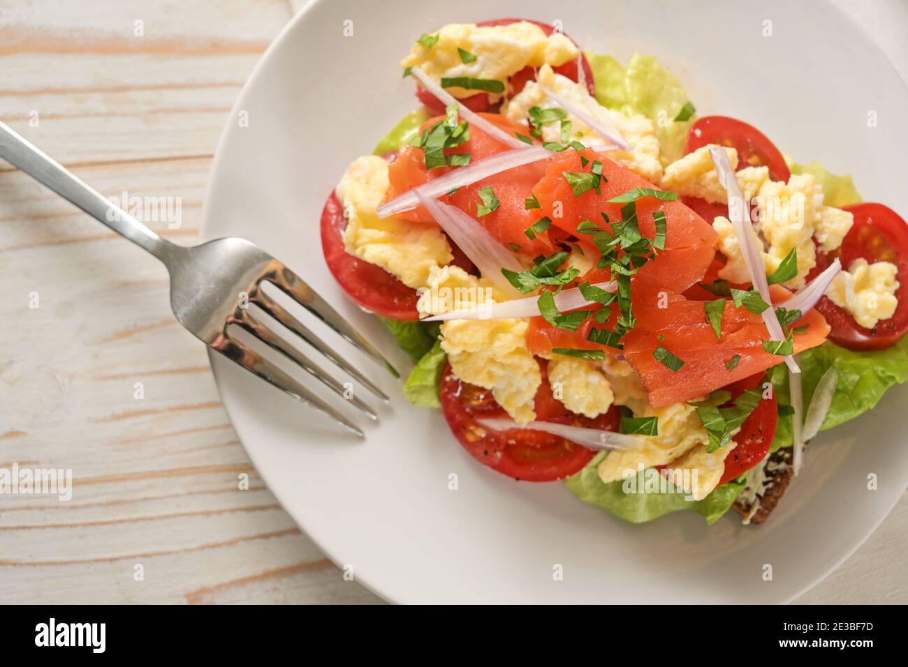 Smoked salmon and scrambled eggs with onion and parsley garnish on whole meal bread with tomatoes and lettuce, healthy sandwich snack on a white plate Stock Photo