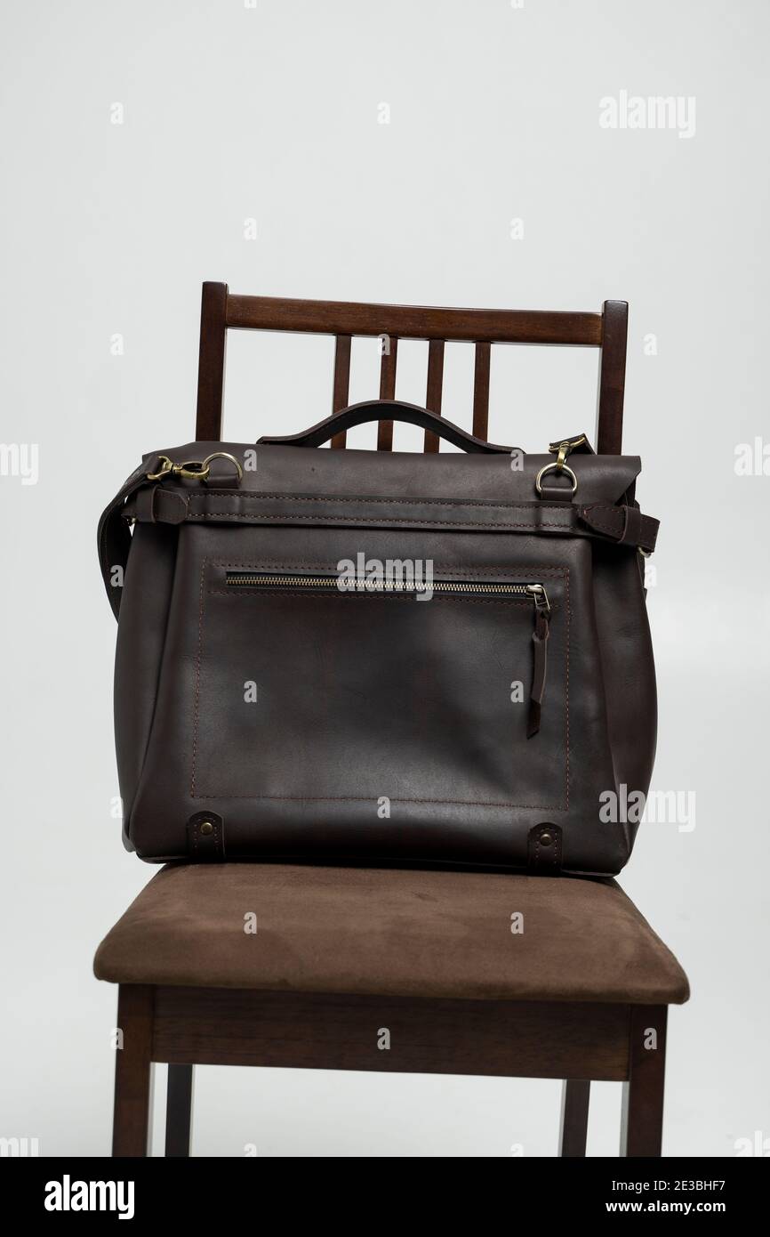Brown men's shoulder leather bag for a documents and laptop on a brown chair with a white background. Mens leather brief case, messenger bags, leather Stock Photo