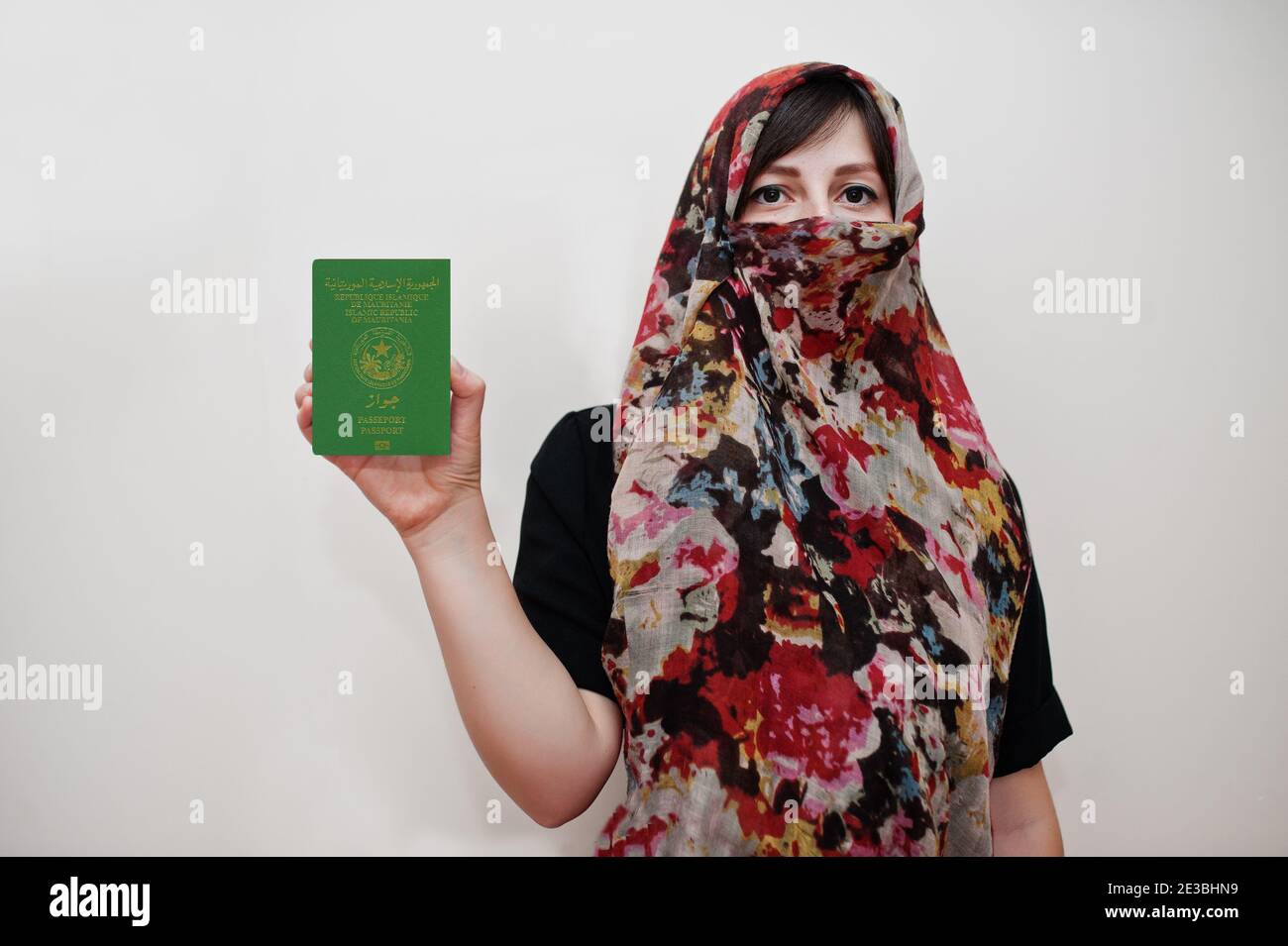Young arabian muslim woman in hijab clothes hold Islamic Republic of Mauritania passport on white wall background, studio portrait. Stock Photo