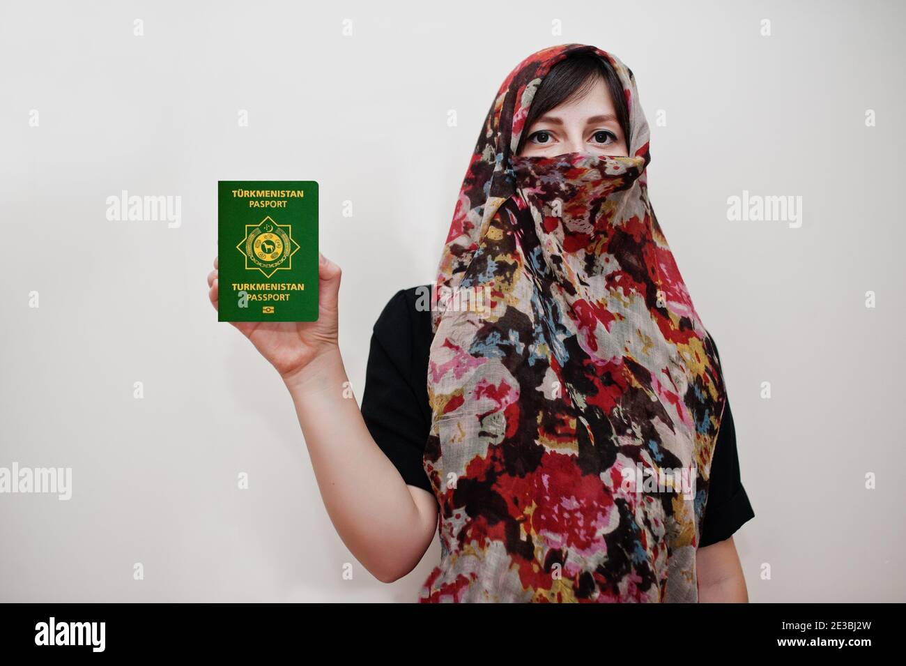 Young arabian muslim woman in hijab clothes hold Turkmenistan passport on white wall background, studio portrait. Stock Photo