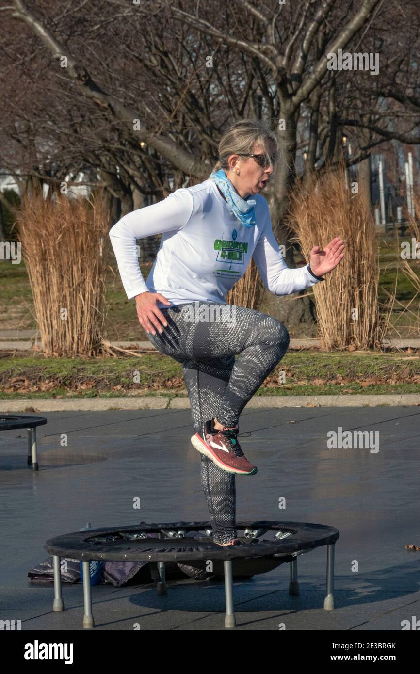 A woman at a rebounding class which combines vigorous movements while jumping on a small trampoline. In flushing Meadows Corona Park in Queens, NYC. Stock Photo