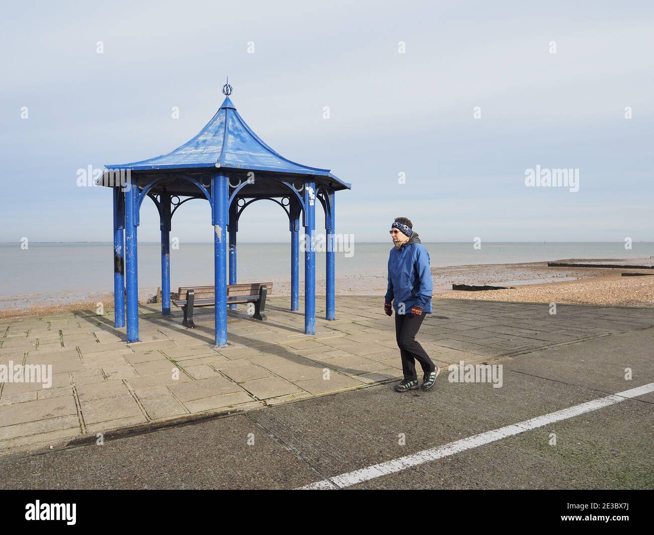 Sheerness, Kent, UK. 18th January, 2021. UK Weather: blue Monday in Sheerness, Kent - a cold day with some sunny spells. A woman in a blue coat walks past a blue seafront shelter on blue Monday. Credit: James Bell/Alamy Live News Stock Photo