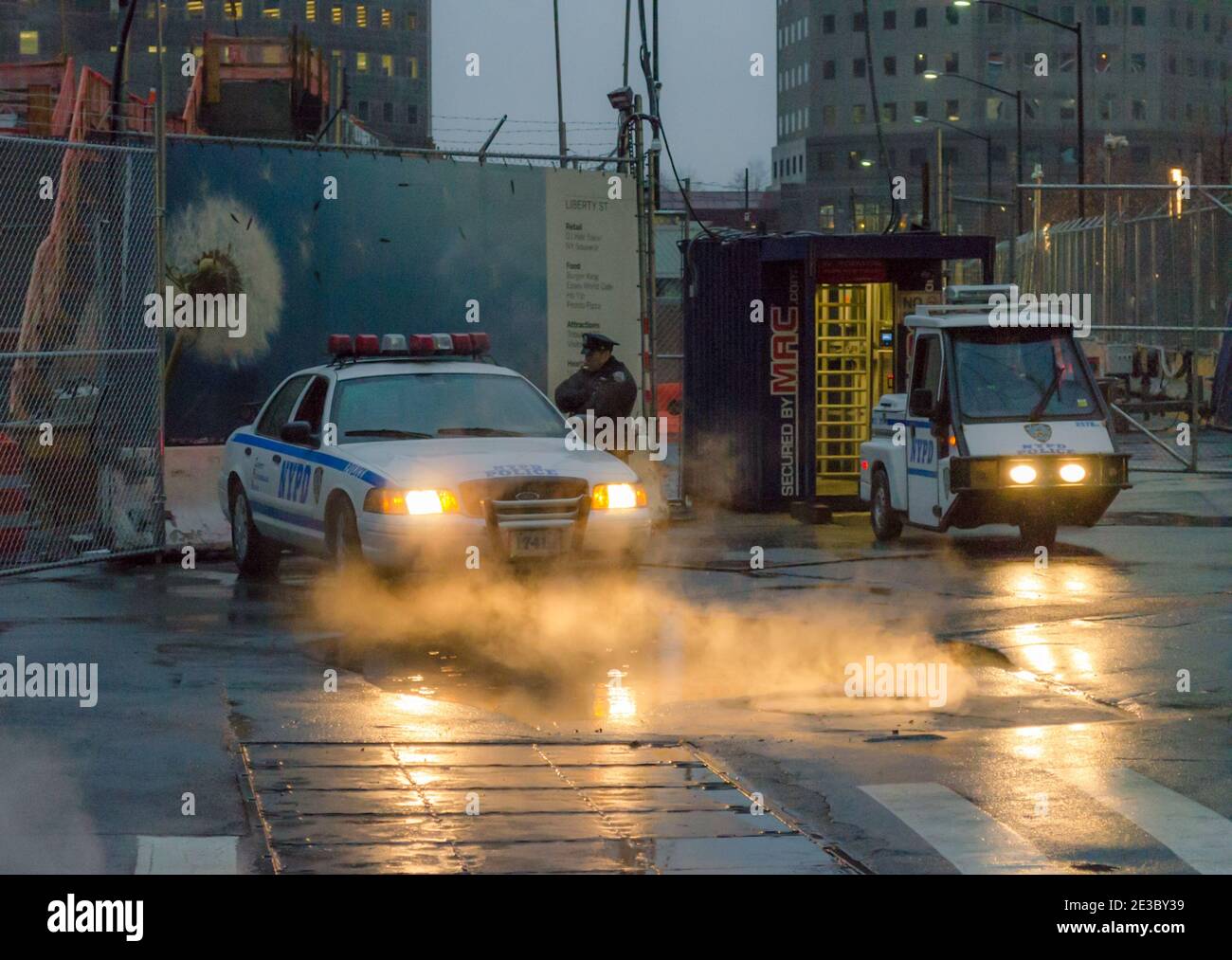 An Officer and a Police Vehicle with its Headlights Shed Light on Steam Coming from the Sewers in Lower Manhattan, New York City, USA Stock Photo