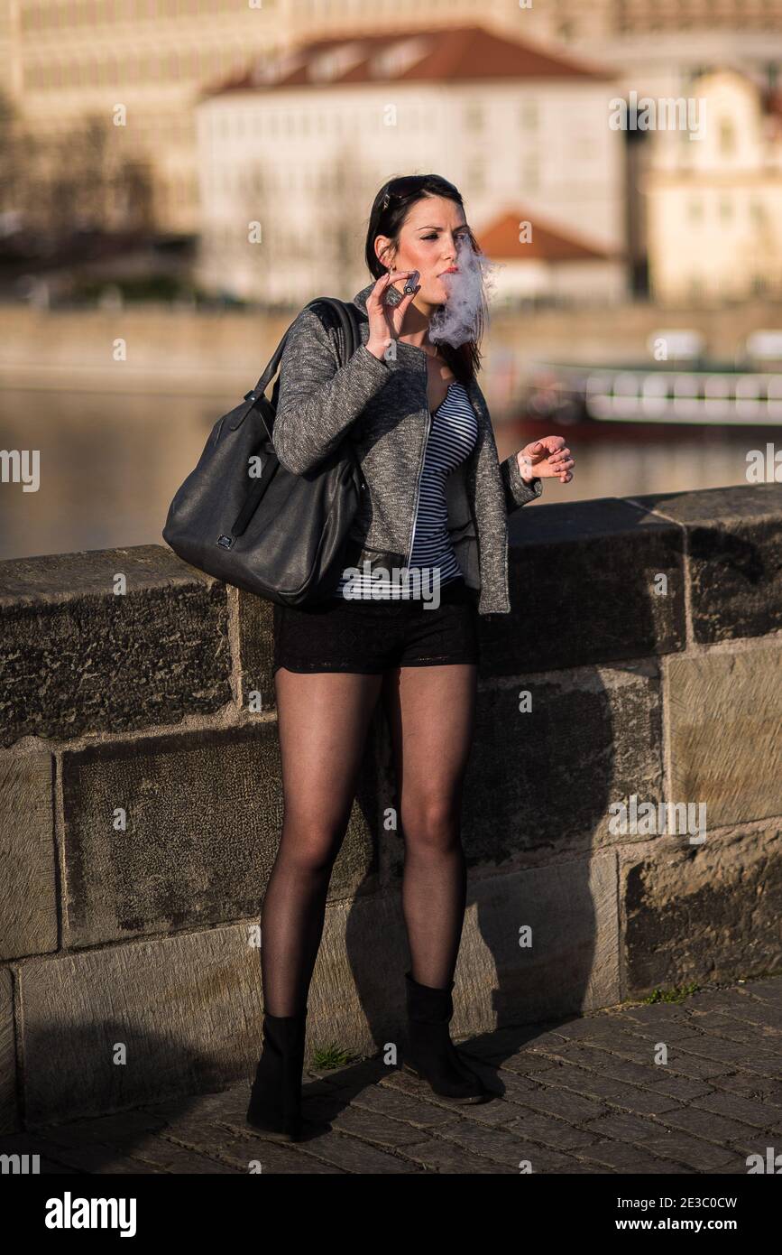 Prague, Czech Republic. 09-23-2019. Young woman smoking electronic cigarette on the Charles Bridge during a sunny day in Prague. Stock Photo