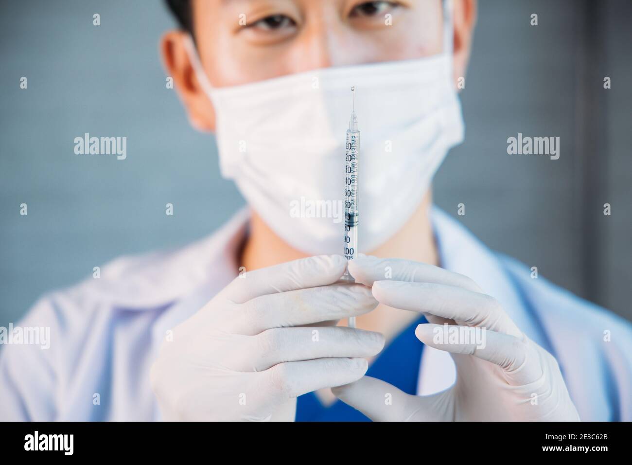 Close up of male Asian doctor holding a vaccine injection needle ready for vaccination. Young lab technician scientist at work Stock Photo