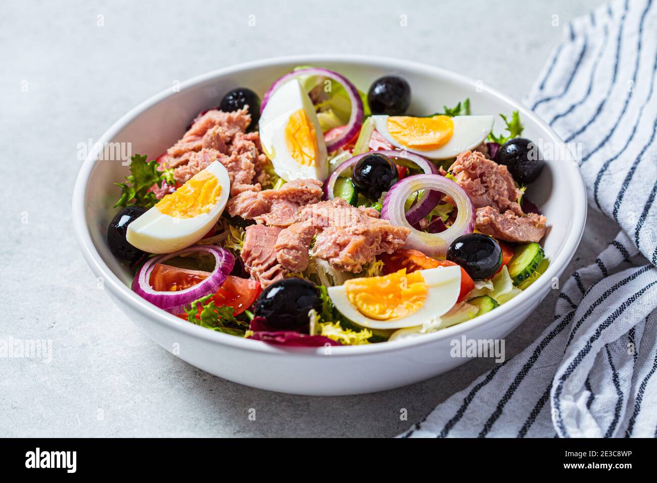 Tuna salad with egg, olives and vegetables in a white bowl, white background. Diet food concept. Stock Photo