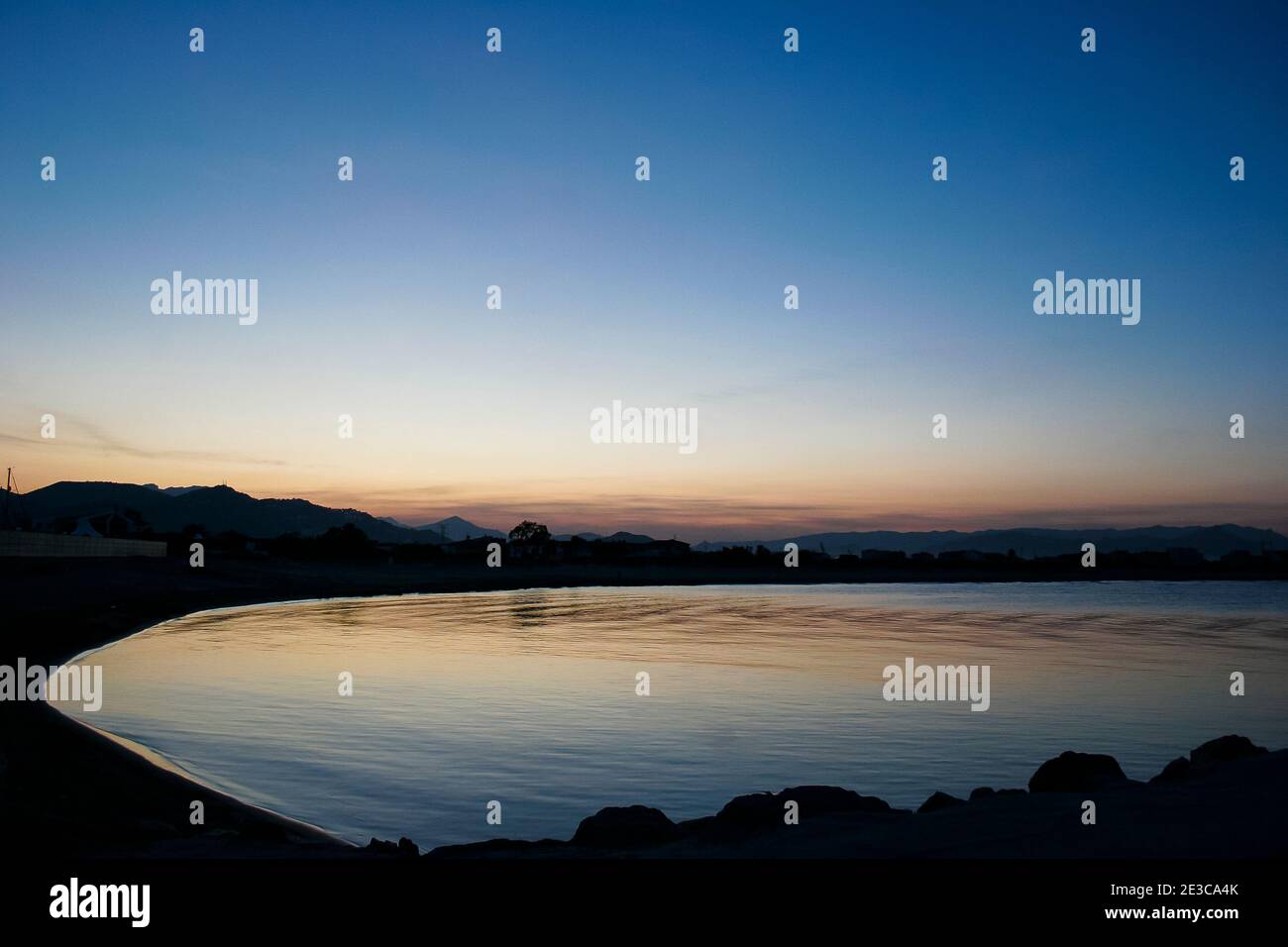 The sun setting over the mountains with views over a calm still bay in Oliva, Spain Stock Photo