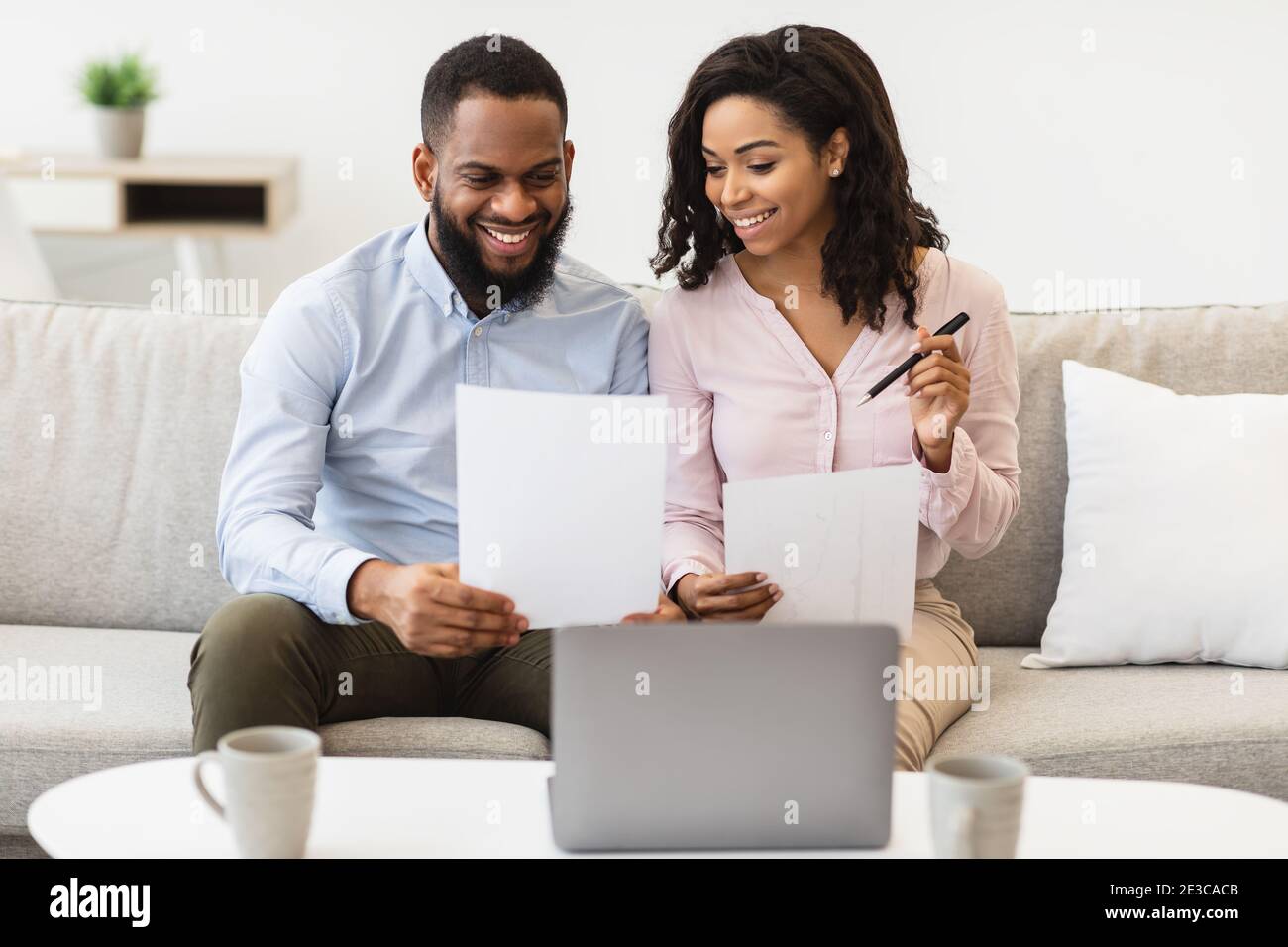 Cheerful black couple reading documents at home, checking bills Stock Photo