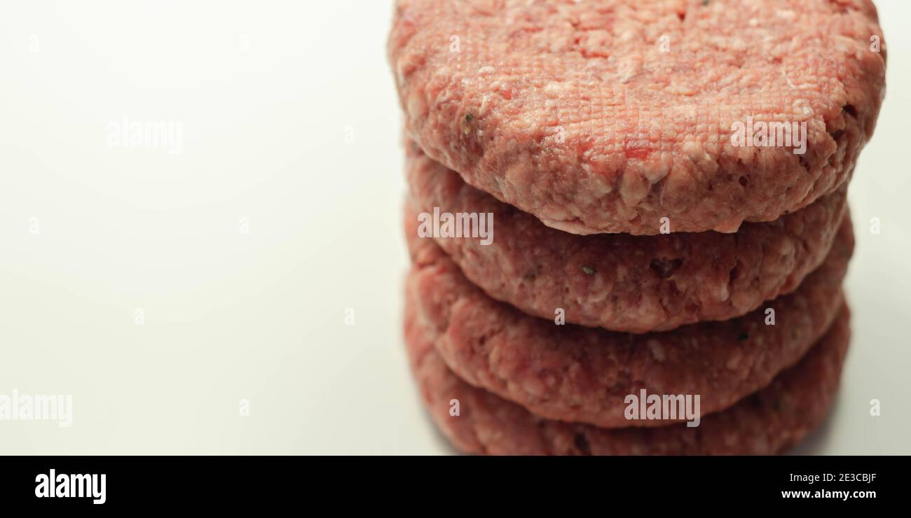 Raw beef burgers with a pinch of salt and black pepper on the white