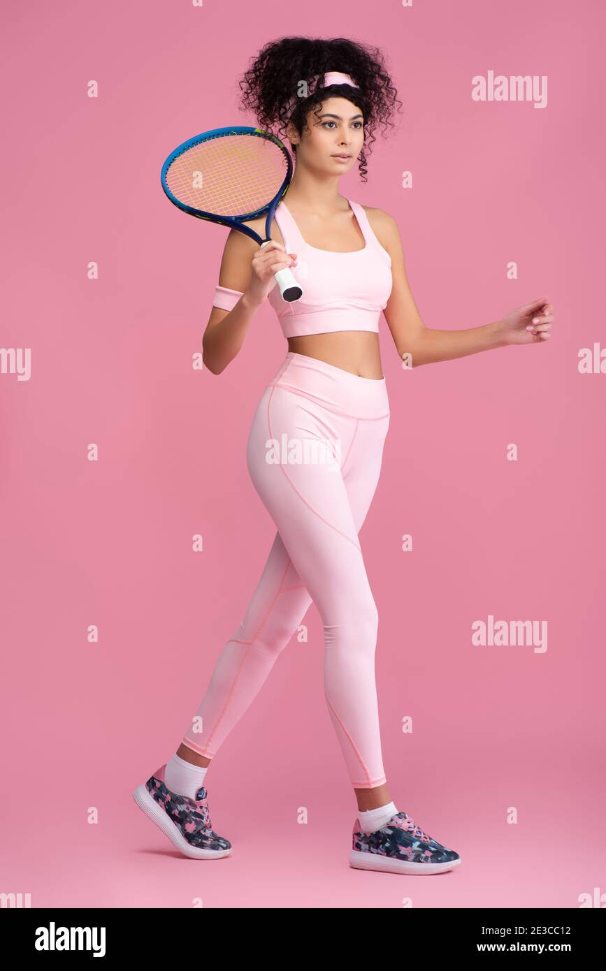 full length of young curly sportswoman holding tennis racket while ...
