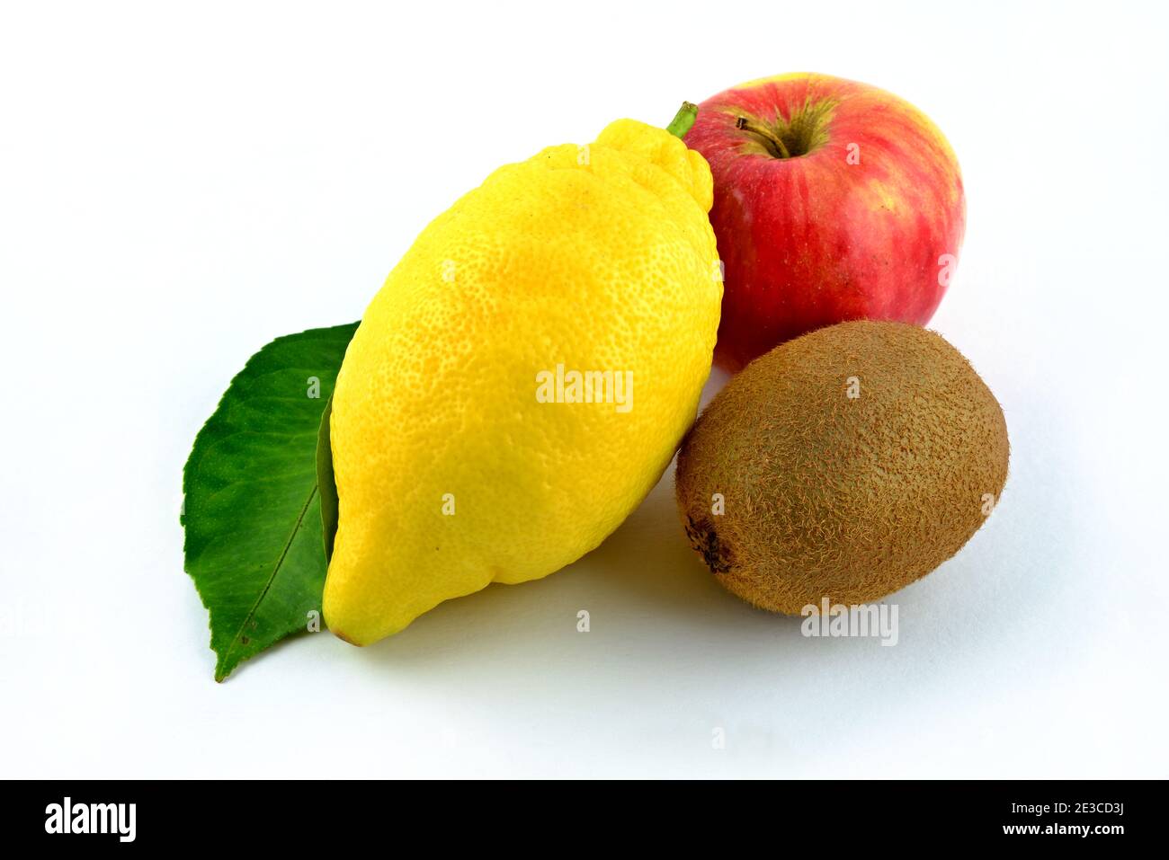 Mixture of fruits, one yellow lemon, one red apple, one brown kiwi. Green lemon leaf. Stock Photo