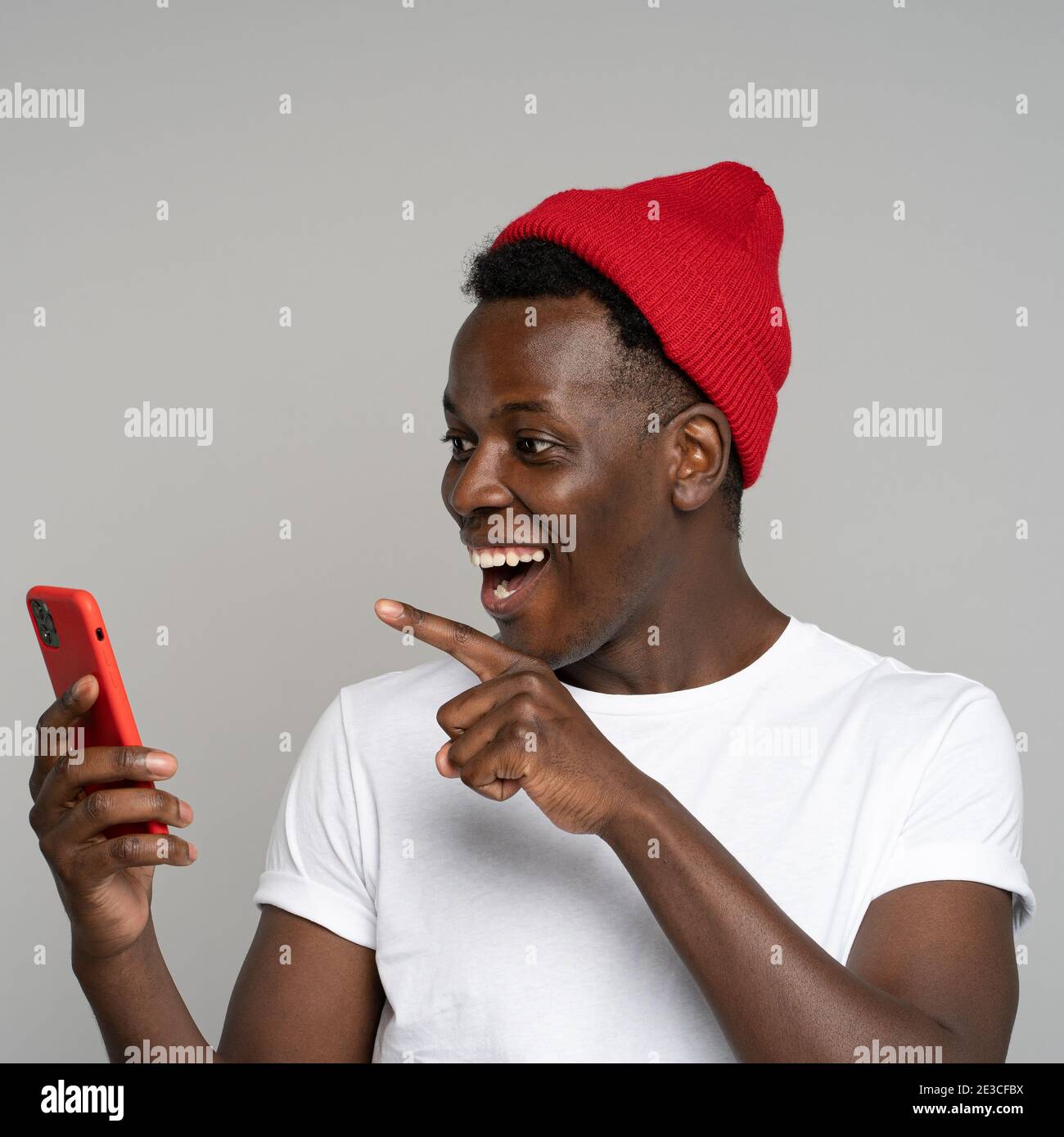 Surprised African hipster man talking in video chat pointing finger on screen mobile phone, isolated Stock Photo