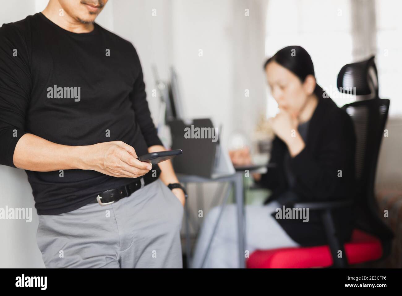 Businessman using mobile phone while woman working in background. Stock Photo