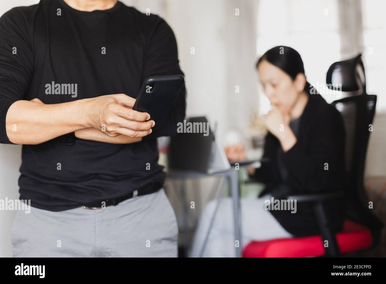 Businessman using mobile phone while woman working in background. Stock Photo
