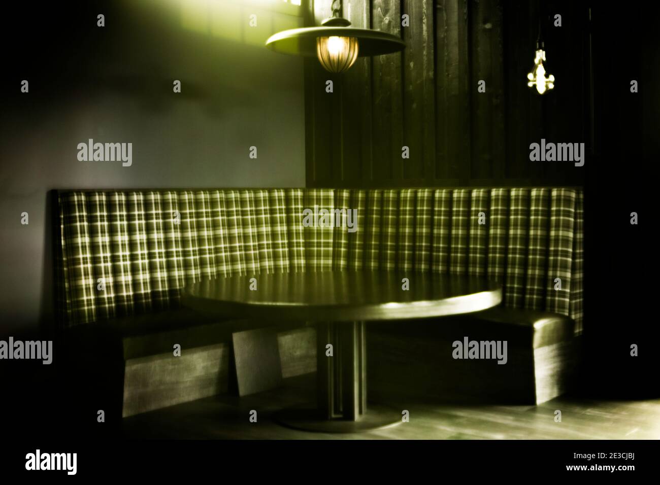 A corner booth flanking a round wooden table shot in ultraviolet light; giving the image a green cast. Stock Photo
