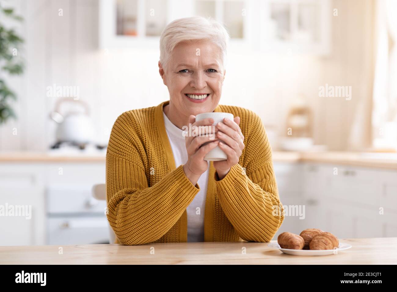 Cheerful elderly lady drinking tea with croissant Stock Photo
