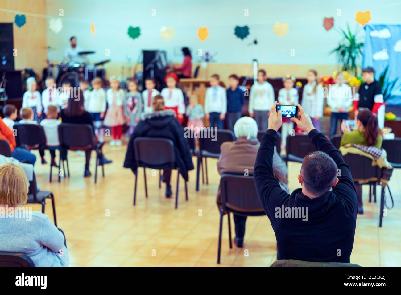 Parents at the performance of children in kindergarten or school. Children on stage. Many parents are watching the kids performance in the hall during Stock Photo
