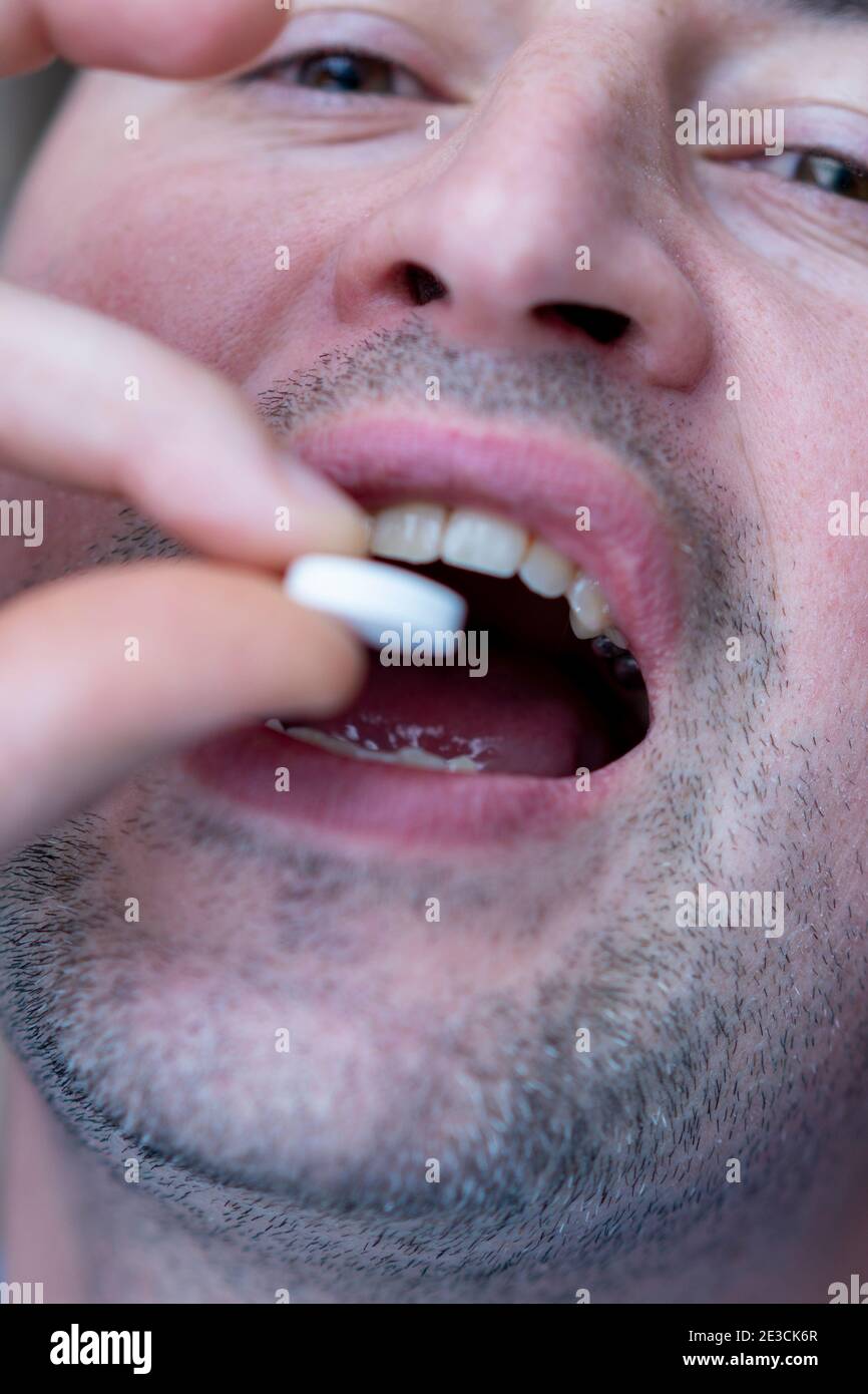 Extreme closeup man face taking white pill, mouth view swallowing pills, illness. man take medicine,open mouth and bring medicine to mouth. toned Stock Photo