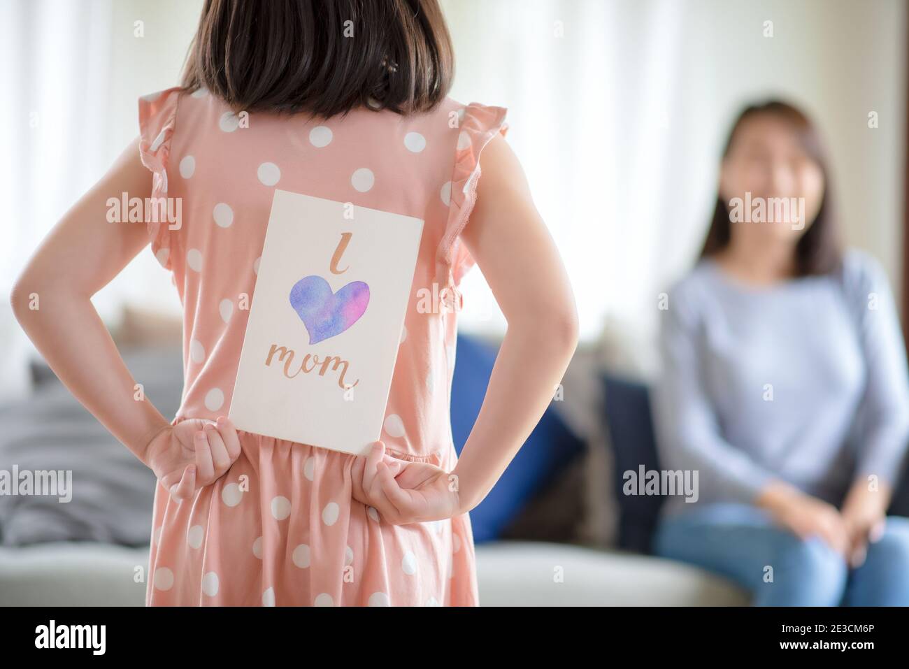 Asian cute girl hide handmade greeting card with i love mom word to give surprising her mother at home Stock Photo