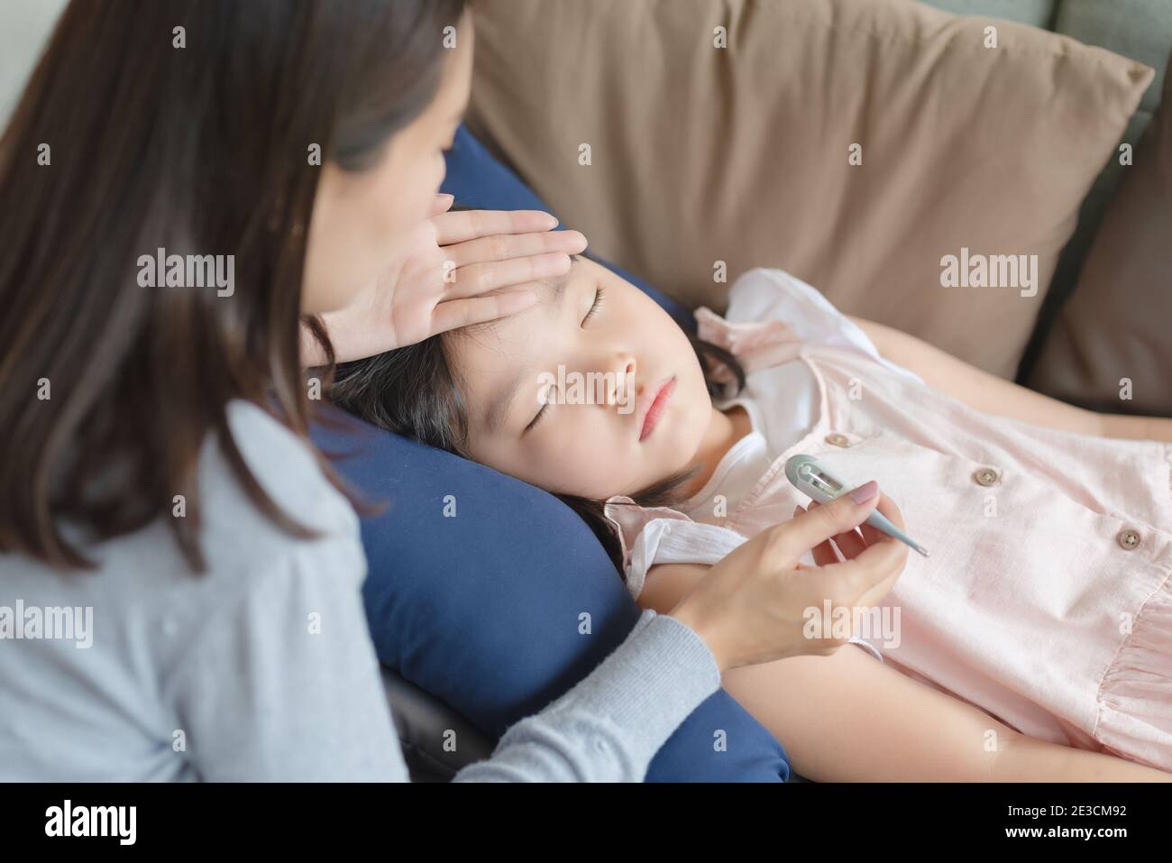 Asian mother checking her kid body temperature by thermometer which got fever and illness at home. Stock Photo