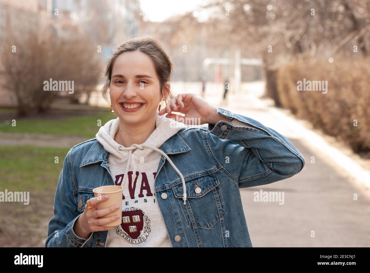 Young caucasian girl happy smiling and drinking coffee in outdoor. Young happy girl holding a paper cup of coffee. Stock Photo