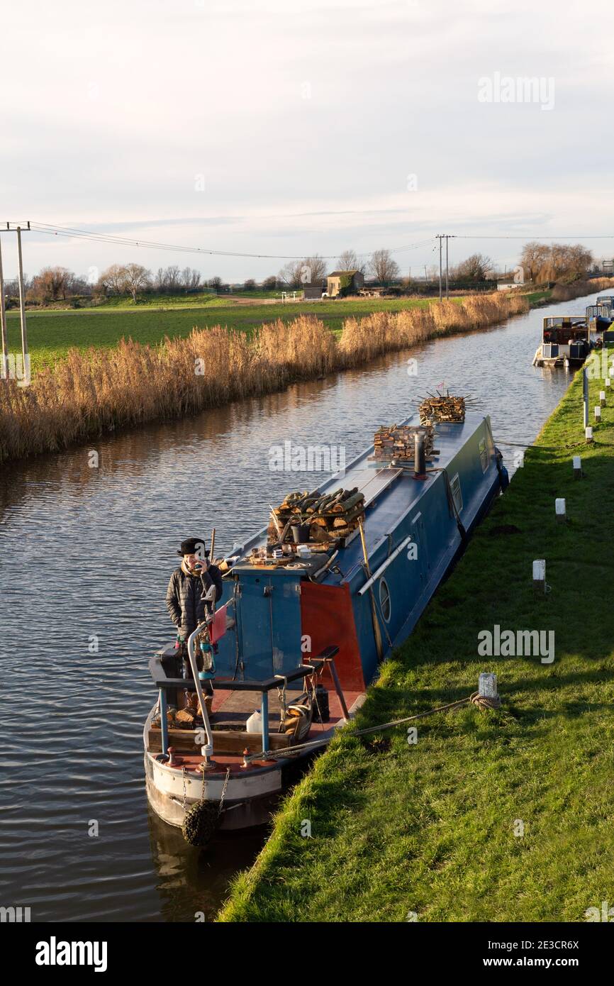A woman living on a canal boat or narrow boat moored on the fens at Upware in winter, Cambridgeshire UK; example of lifestyle, living on a boat. Stock Photo