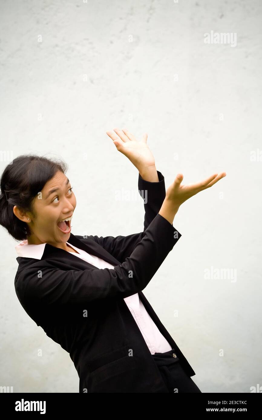Pretty Asian businesswoman seems to be surprised going to catch something (can be a reward, bonus, prize, etc.) that is going to fall on her. Stock Photo