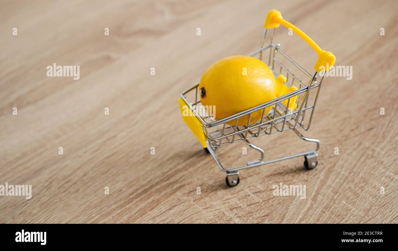 Lemon in a supermarket cart on kitchen table wooden background