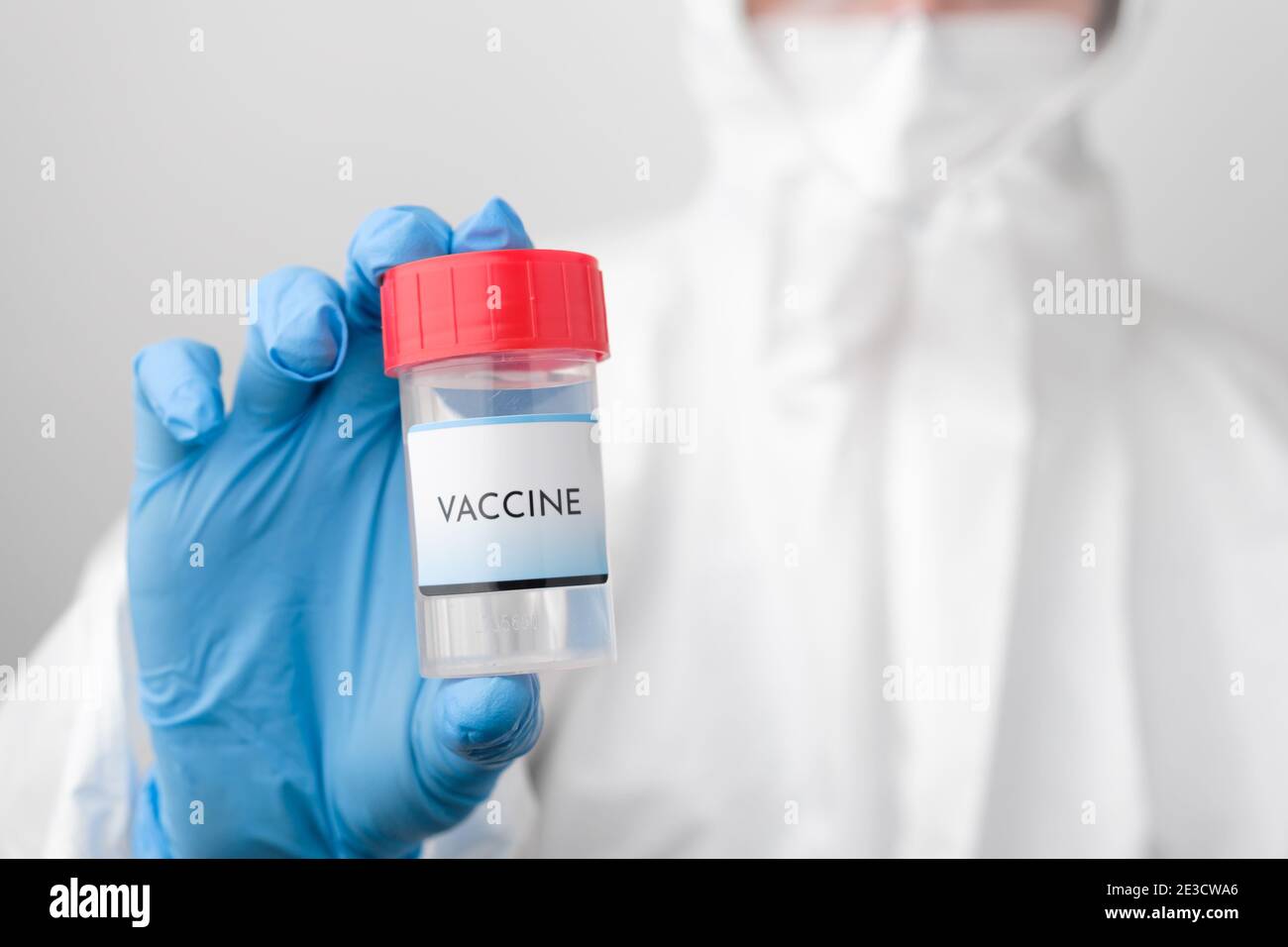 Covid 19 vaccine bottle in doctors hand. Doctor in protective suit, face mask, safety googles and rubber gloves demonstrate vaccine against Stock Photo