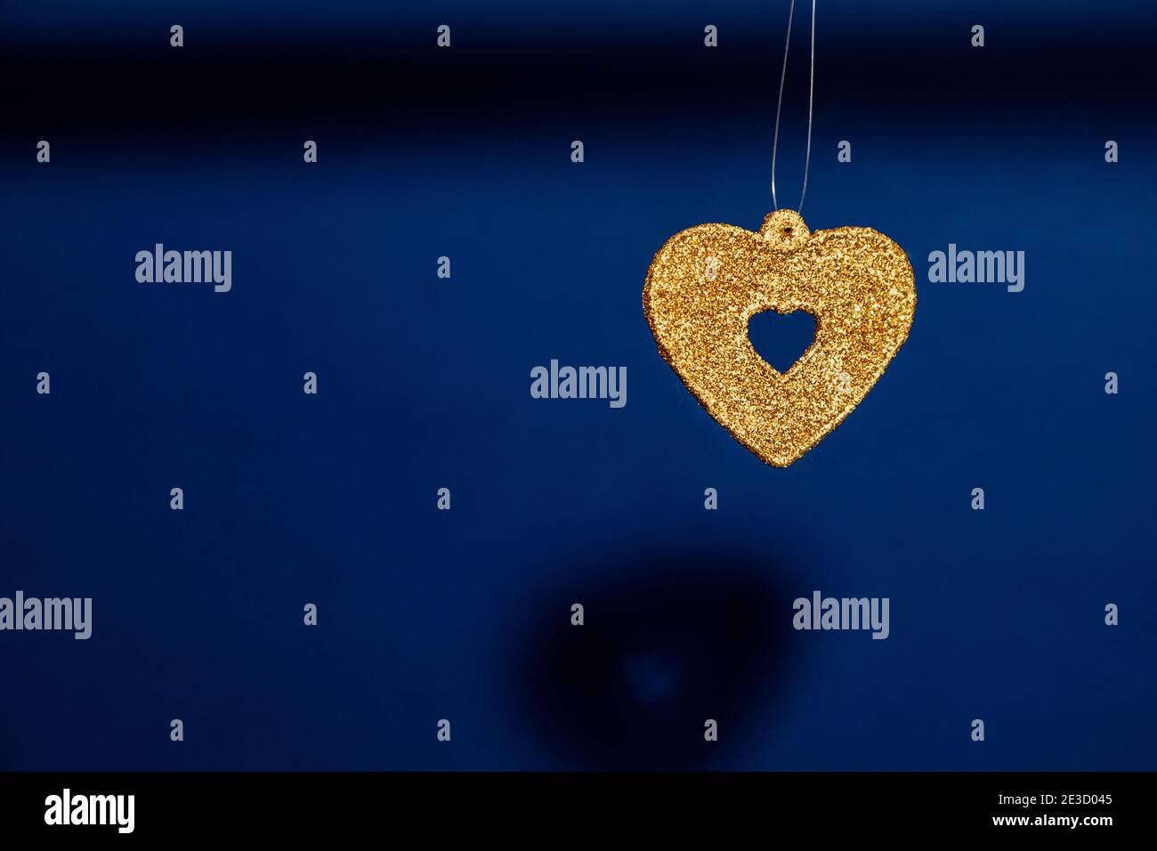 sparkly gold heart hanging in front of a blue background Stock Photo