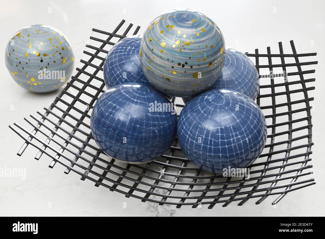 Blue glass orbs and a wire mesh bowl on a white background Stock Photo
