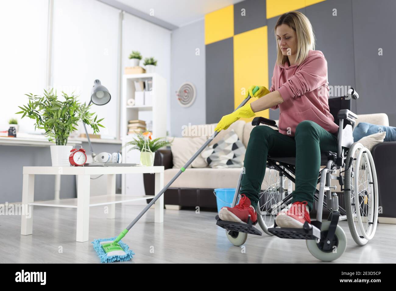 Woman in wheelchair washes the floor with mop Stock Photo