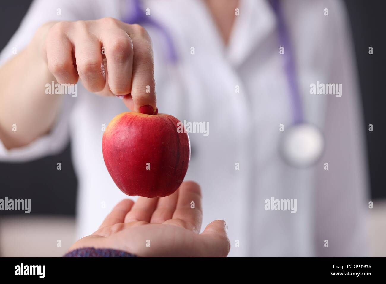 Doctor hands over a ripe apple to the patient. Anti-aging treatments Stock Photo