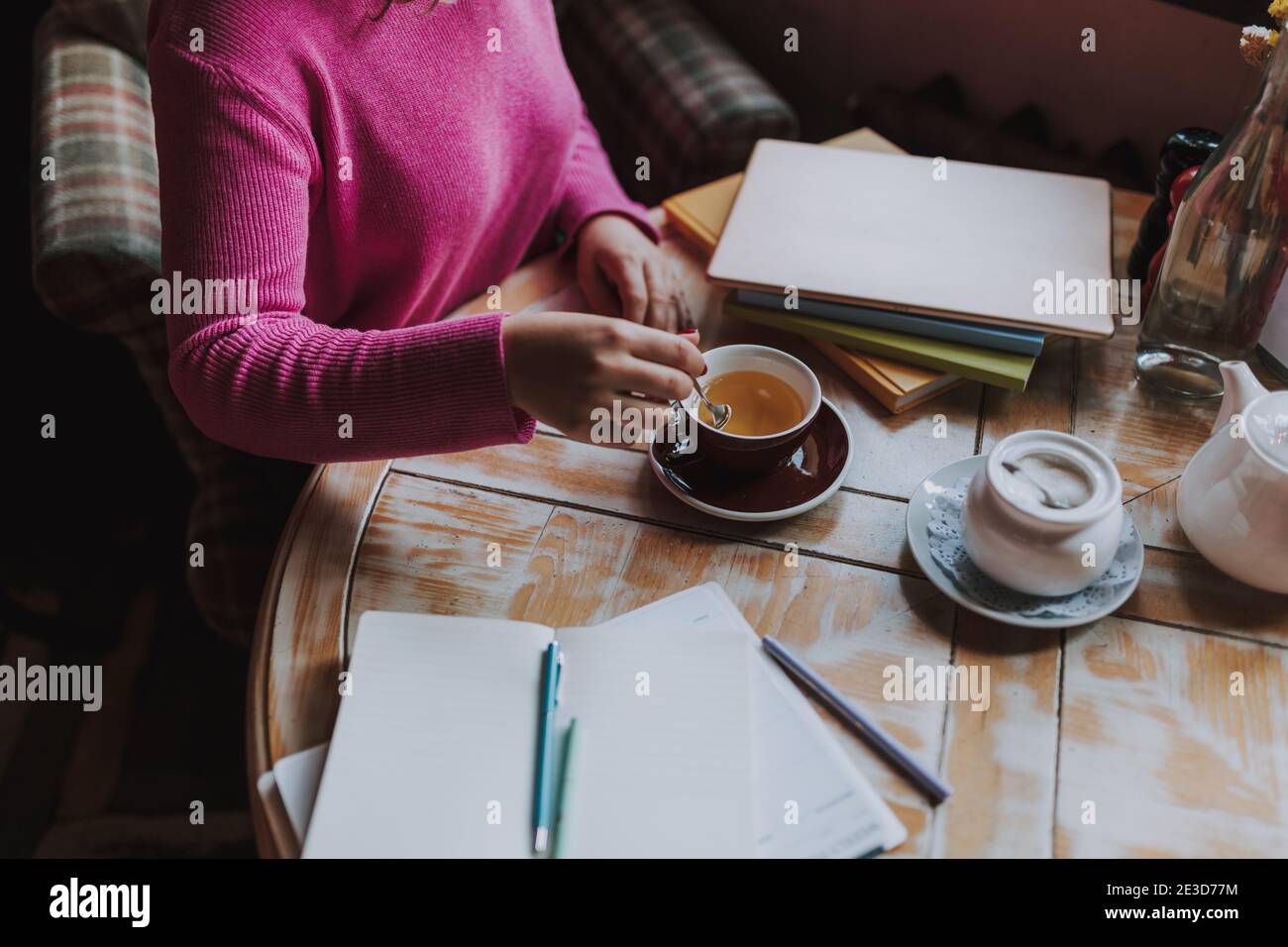 Top view of young lady studying in cafeteria and enjoying hot drink while stirring tea with a teaspoon Stock Photo