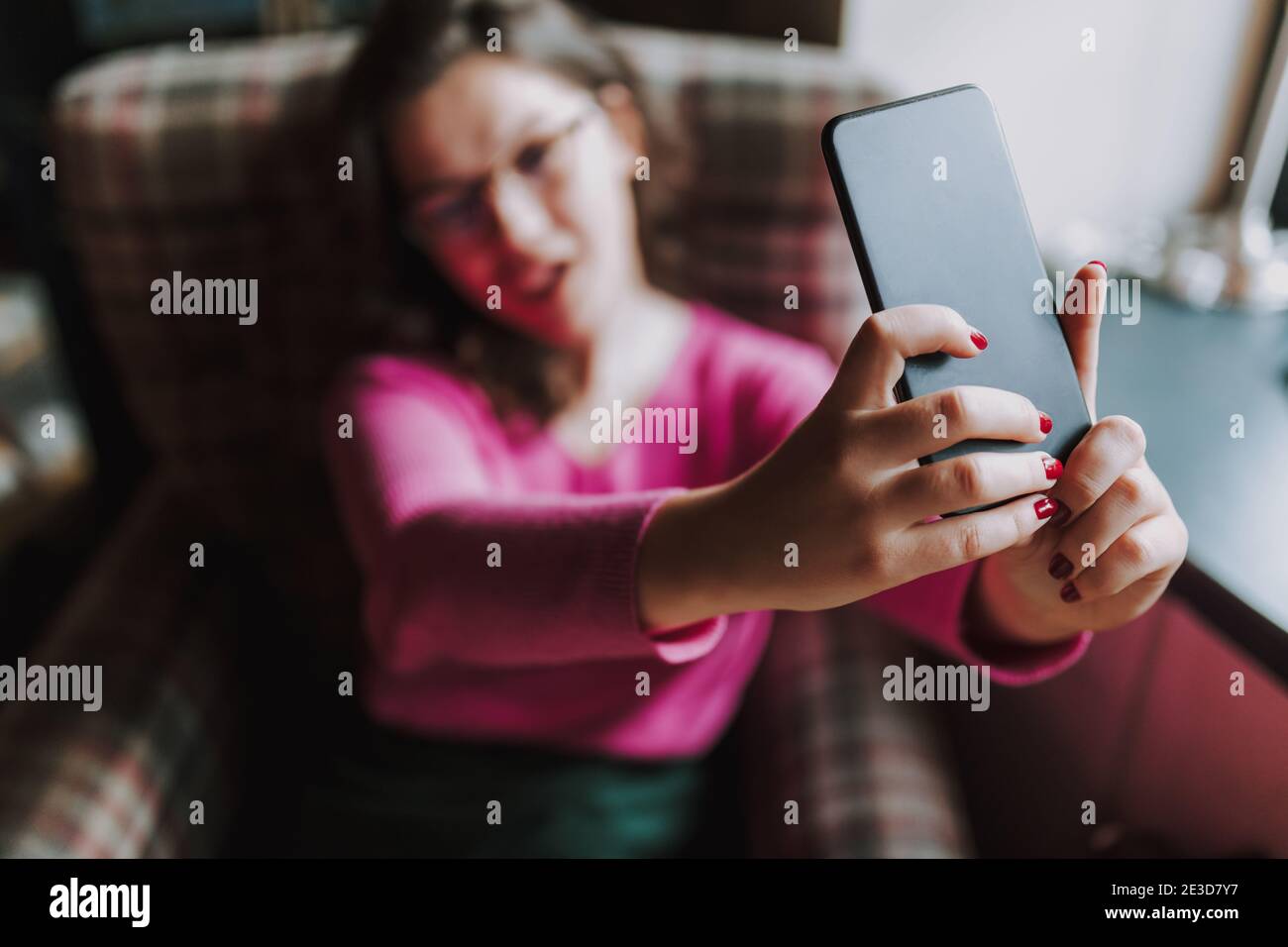 Smiling young lady posing on smartphone camera while taking selfie in cafe Stock Photo